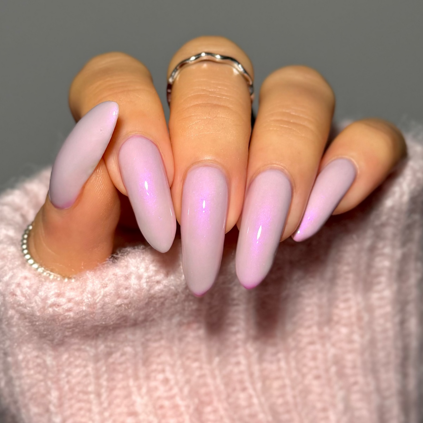 Hand with pink and purple gradient nails wearing a light pink sweater.